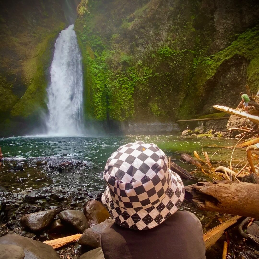 A quiet waterfall scene with a person in a checkerboard hat seen from behind